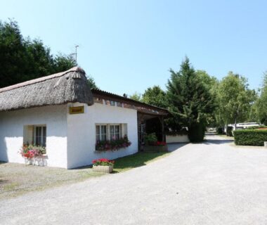 Entrée du camping avec bâtiment d'accueil et toit de chaume au Camping la Chaumière