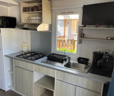 Cuisine équipée avec plaques gaz évier micro-ondes télévision dans un hébergement au Camping la Marine