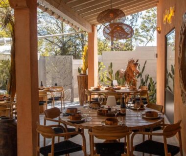 Terrasse couverte avec tables en bois et luminaires en osier au Camping la Peiriere - Évasion en Dôme