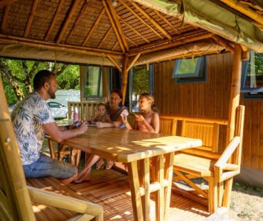 Terrasse couverte avec table et famille au Camping la Plage Lot Vallée de la Dordogne Rocamadour