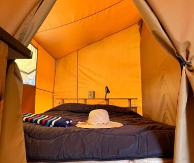 Intérieur de tente glamping avec lit et chapeau au Camping la Tamarissière