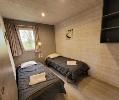 Chambre avec deux lits simples et serviettes près de la fenêtre au Camping la Venise Verte