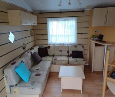 Salon avec canapé d'angle table basse et kitchenette dans le Camping le Bois Jahan
