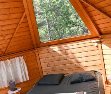 Intérieur de cabane en bois avec lit et fenêtre sur les arbres au Camping le Colorado