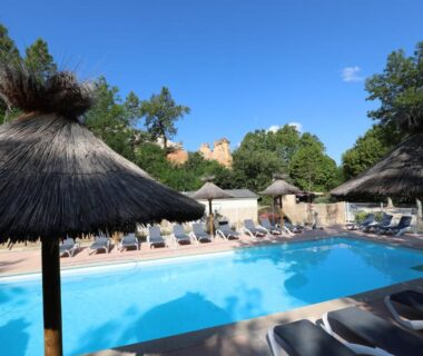 Piscine extérieure bordée de transats et parasols en paille au Camping le Colorado