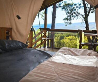 Intérieur de tente avec lits et terrasse donnant sur plan d'eau au Camping le Colorado