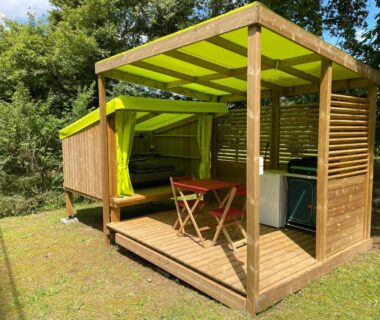 Terrasse couverte en bois avec banquette et kitchenette au camping le Convivial Cop'Camp 2 personnes