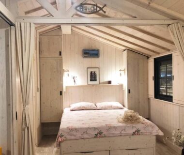 Chambre en boiserie blanche avec lit double et rideaux au Camping le Marache