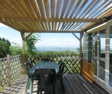 Terrasse ombragée avec table et chaises offrant vue sur la campagne au Camping le Montbartoux