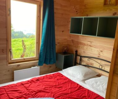 Chambre en bois avec lit et fenêtre donnant sur la campagne au Camping le Montbartoux