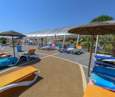 Espace piscine couvert avec transats et parasols au Camping le Moulin de la Salle
