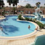 Piscine extérieure avec toboggan et palmiers au Camping le Neptune