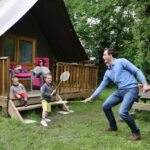 Devant le chalet famille jouant au badminton au Camping le Nid du Parc
