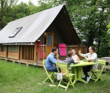 Devant un chalet en bois avec table et famille au Camping le Nid du Parc