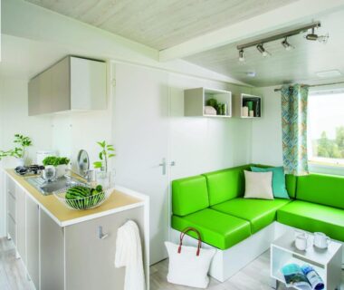 Coin salon avec canapé vert et kitchenette dans un mobil-home au Camping le Rancho