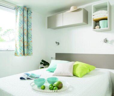 Chambre avec lit double coussins verts et fenêtre au Camping le Rancho
