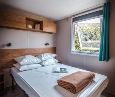 Chambre avec lit double et fenêtre donnant sur jardin au Camping le Roucan West