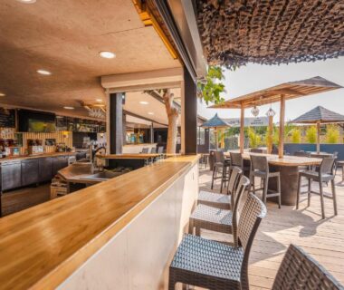Terrasse extérieure avec bar tables et parasols du Camping le Roucan West