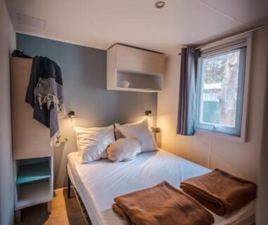 Chambre intérieure avec lit double couvertures et fenêtre dans l'hébergement du Camping le Roucan West