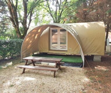 Dans un emplacement ombragé une tente lodge et une table de pique-nique au Camping le beauvillage Lauzerte