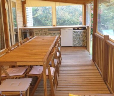 Terrasse couverte en bois avec table à manger et chaises au Camping les Cigales Tikayan