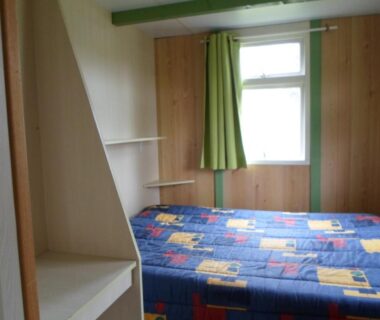 Intérieur de la chambre avec lit double panneaux en bois et rideau vert au Camping les Pinasses