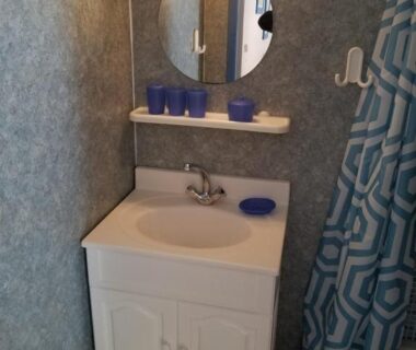 Lavabo avec miroir et rideau de douche dans le sanitaire du Camping les Tourterelles Chalets et mobilhomes