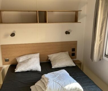Chambre avec lit double étagères et fenêtre dans le mobil home 6 personnes Camping les dunes 5 étoiles