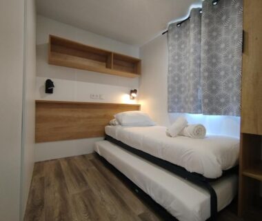 Chambre avec lit gigogne, rangements et rideaux dans le camping Les Lodges du Lagon