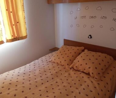 Chambre avec lit double couette à pois et rideaux jaunes au Camping l'escale