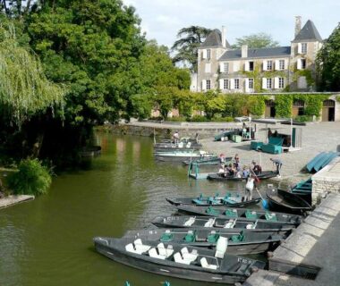Bord de rivière avec barques amarrées devant une demeure au Camping l'île Cariot