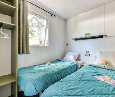 Chambre avec deux lits et fenêtre donnant sur végétation au camping maeva Escapades Millau Plage
