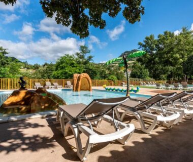 Piscine extérieure avec jets d'eau et transats au Camping maeva Escapades Millau Plage