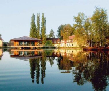Bord du lac et bâtiments en reflet au Camping maeva Respire Domaine de Sainte Montaine