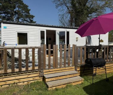 Terrasse en bois avec parasol et barbecue devant un mobil-home au Camping paradis