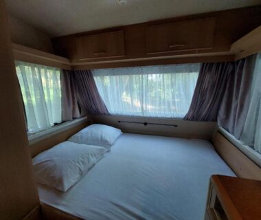Intérieur chambre avec lit et fenêtres dans la caravane La Clairière