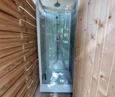 Couloir extérieur avec cabine de douche en verre de la Caravane La Clairière