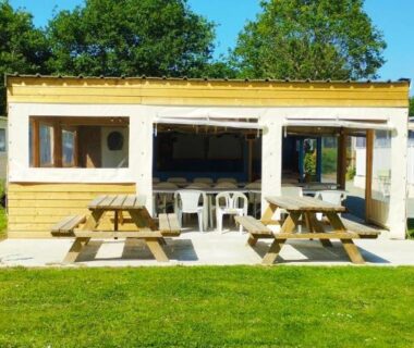 Terrasse extérieure avec tables de pique-nique sur pelouse devant bâtiment du camping Caravane vintage