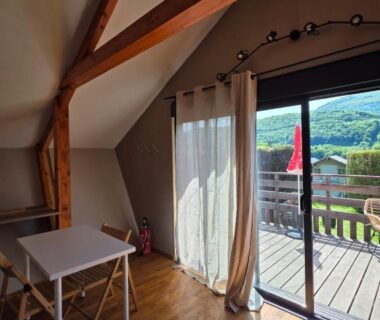 Intérieur mansardé avec table et terrasse donnant sur la vallée du Chalet avec piscine 2C