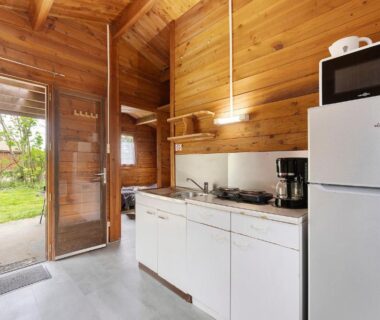 Intérieur kitchenette en bois avec porte vitrée donnant sur jardin dans le Chalet bois 8 Domaine Les Epinettes