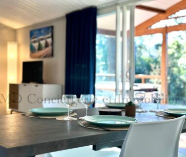 Séjour avec table dressée près de baie vitrée donnant sur terrasse du Chalet en bord de plage