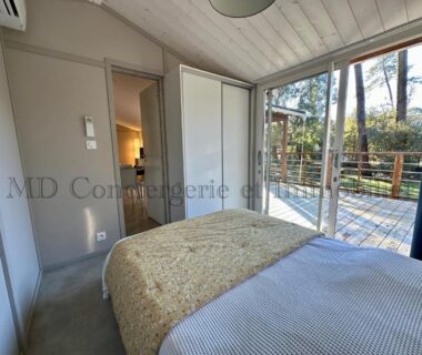 Chambre avec baie vitrée ouvrant sur terrasse en bois et pinède du Chalet en bord de plage
