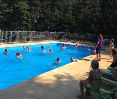Piscine extérieure avec enfants et adultes dans un cadre boisé au Camping les Sapins