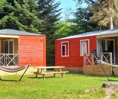 Pelouse avec deux chalets en bois et hamacs au Camping les Sapins