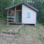 Chalet en bois entouré de sous-bois avec terrasse et escaliers au Chalet nature et lac dans parc résidentiel de loisirs
