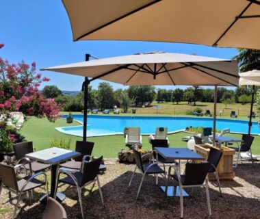Terrasse ombragée avec tables et chaises au bord de la piscine aux Chalets de l'Oasienne