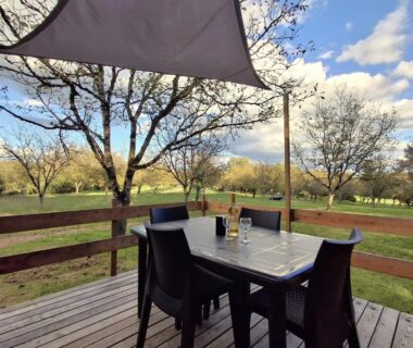 Terrasse en bois avec table et chaises donnant sur pelouse aux Chalets de l’Oasienne