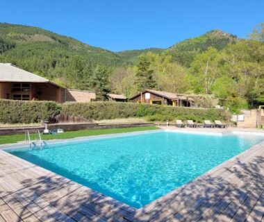 Piscine extérieure bordée de dalles et chalets au camping Chanteduc