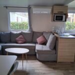 Salon avec canapé et kitchenette du Charmant mobil-home N°698 3ch tout confort au calme