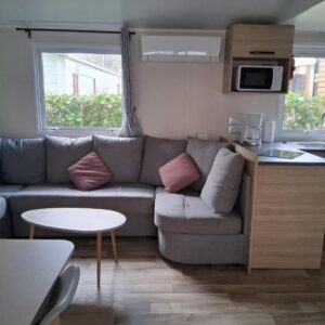 Salon avec canapé et kitchenette du Charmant mobil-home N°698 3ch tout confort au calme